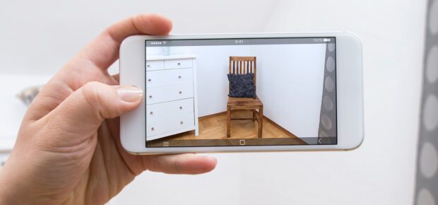 Woman holding a mobile phone using an augmented reality application to see a new chair for the empty corner of the room.