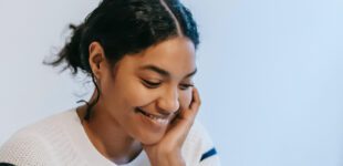 Smiling young ethnic woman working distantly on laptop and talking on smartphone