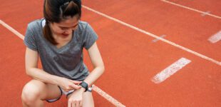 Asian female runner checking health status and fitness progress on her smart watch during exercise in running track.
