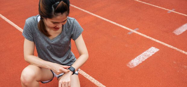 Asian female runner checking health status and fitness progress on her smart watch during exercise in running track.