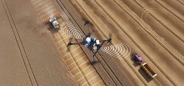 Overhead aerial view of a drone communicating with a combine harvester and tractor while harvesting a crop