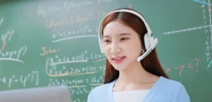 Young woman on headset using computer in front of chalk board