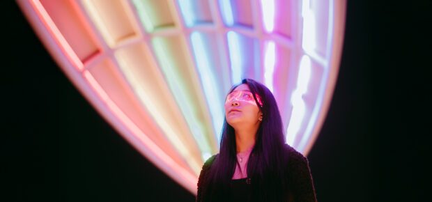 Confident Asian businesswoman wearing glowing glasses on a brightly lit street at night